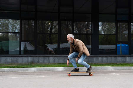 full length of middle aged man in sunglasses riding longboard near buildingの写真素材