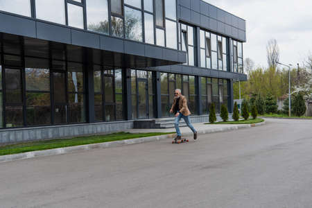 full length of middle aged man in sunglasses riding longboard outsideの写真素材