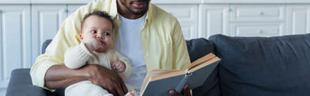 african american man reading book to infant daughter, bannerの写真素材