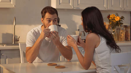 bearded man drinking coffee and looking at blurred girlfriendの写真素材