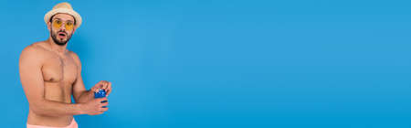 Amazed man in sunglasses holding canned drink isolated on blue, bannerの写真素材