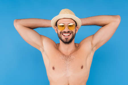 Positive shirtless man in sunglasses and sun hat isolated on blueの写真素材