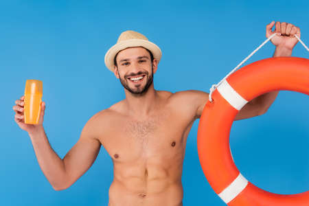 Smiling man holding life buoy and sunscreen isolated on blueの写真素材