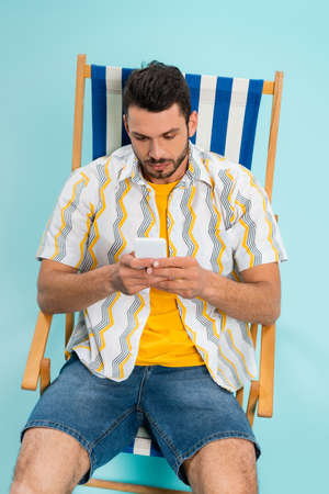 High angle view of young man using smartphone on deck chair on blue background