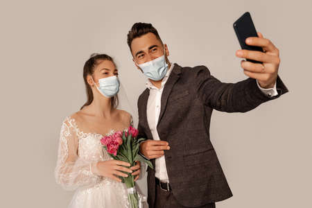 newlyweds in safety masks taking selfie isolated on gray with lilac shadeの写真素材