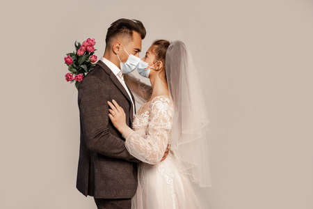 side view of bride and groom in protective masks standing face to face isolated on grayの写真素材