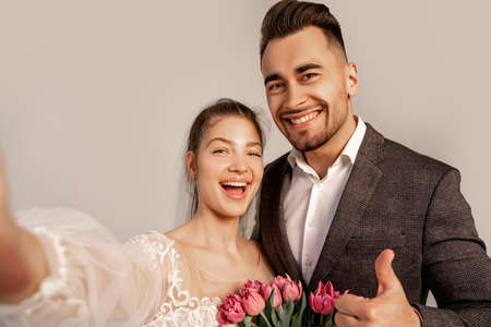 happy man showing thumb up near excited bride isolated on grayの写真素材
