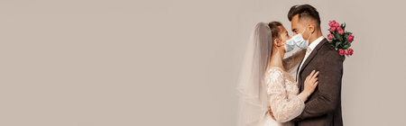 side view of young newlyweds in safety masks standing face to face isolated on gray, bannerの写真素材