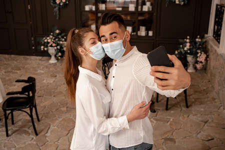 woman in medical mask embracing man taking selfie in restaurantの写真素材