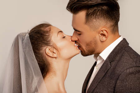side view of young newlyweds kissing with closed eyes isolated on grayの写真素材