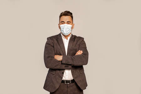 man in suit and medical mask standing with crossed arms isolated on grayの写真素材