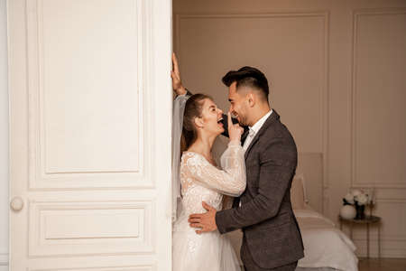side view of laughing bride touching nose of happy groom near entrance to bedroomの写真素材