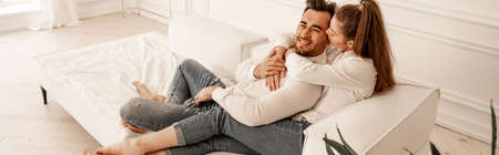 happy young couple in jeans relaxing on sofa at home, banner