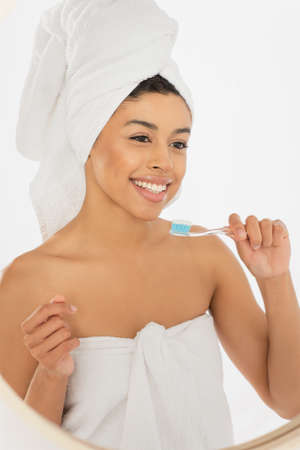 smiling young african american woman wrapped in towels holding toothbrush near face in bathroomの写真素材