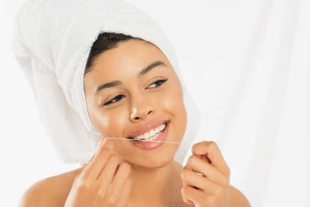 young african american woman wrapped in towel cleaning teeth with dental floss on white background