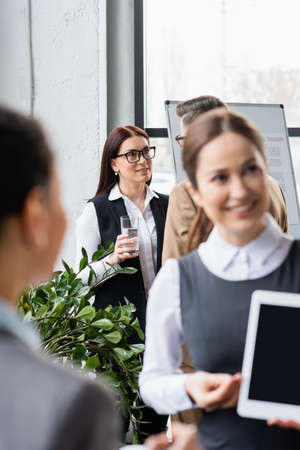 Smiling businesswoman with water talking to colleague near flipchart in officeの写真素材