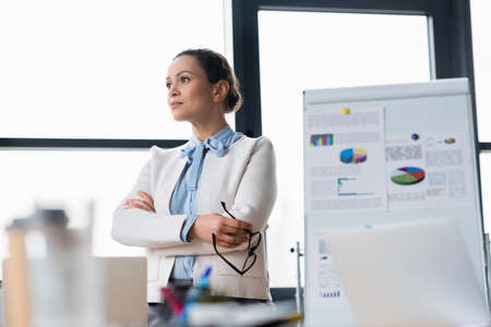 African american businesswoman holding eyeglasses near blurred laptops and flipchart in officeの写真素材