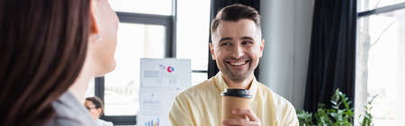 Positive businessman with coffee to go looking at blurred colleague, bannerの写真素材