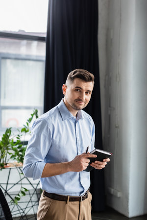 Businessman with pen and notebook looking at cameraの写真素材