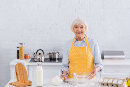 Smiling elderly woman looking at camera near ingredients on kitchen tableの写真素材