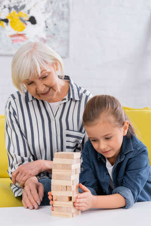Senior woman looking at granddaughter playing blocks wood game at homeの写真素材