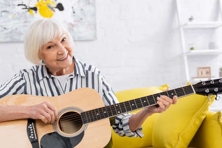 Senior woman with acoustic guitar smiling at cameraの写真素材