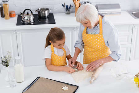 High angle view of girl and grandmother preparing cookie near baking sheet