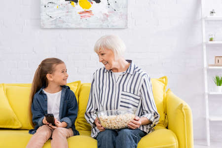 Smiling kid with remote controller looking at granny with popcornの写真素材