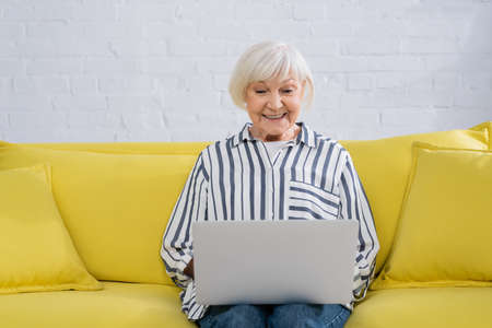 Elderly teleworker smiling and looking at laptop while working from homeの写真素材