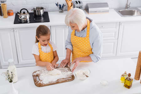 Overhead view of smiling granny helping to child with dough in kitchenの写真素材