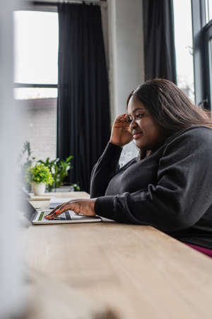 smiling african american plus size woman typing on laptop keyboard in officeの写真素材