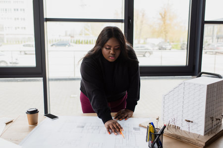 african american plus size designer looking at blueprint on desk with house modelの写真素材