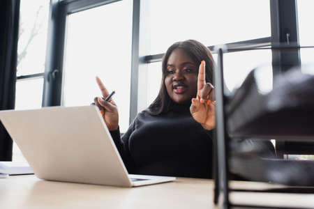 african american plus size businesswoman gesturing while having video call on laptop in office