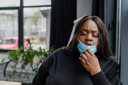 african american plus size businesswoman taking off medical mask while feeling unwell in office