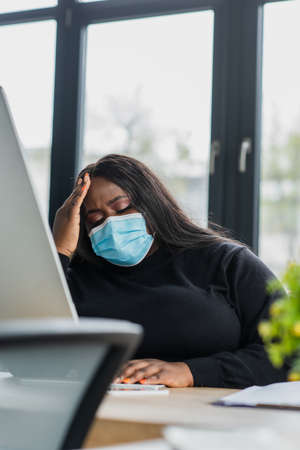 african american plus size businesswoman in medical mask suffering from headache