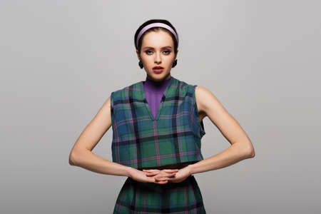 young model in headband, earrings and green checkered outfit posing isolated on grayの写真素材