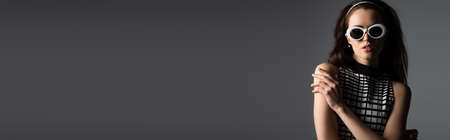 elegant woman in headband and white sunglasses looking at camera isolated on gray, bannerの写真素材