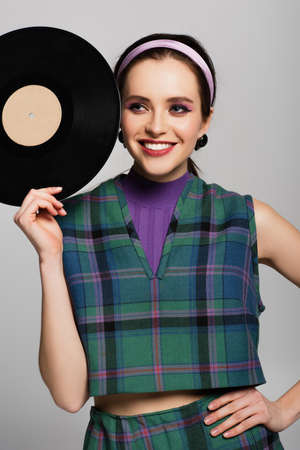 smiling woman in retro outfit holding retro vinyl disc isolated on grayの写真素材