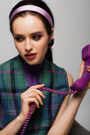 pretty young woman holding purple retro phone isolated on grayの写真素材