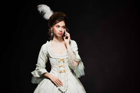 charming woman in elegant retro dress talking on mobile phone isolated on blackの写真素材