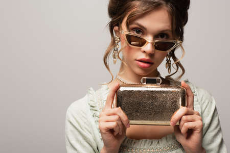 stylish woman in vintage outfit holding golden clutch bag isolated on grayの写真素材