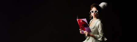 woman in retro outfit and trendy sunglasses holding modern magazine isolated on black, banner