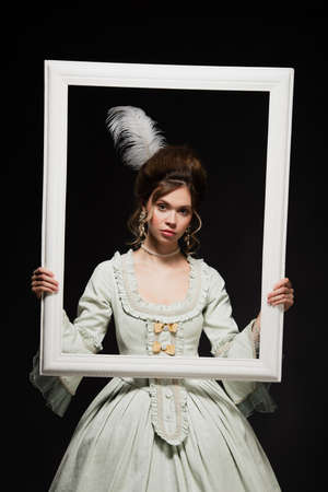 charming woman in elegant vintage outfit holding white framing isolated on blackの写真素材