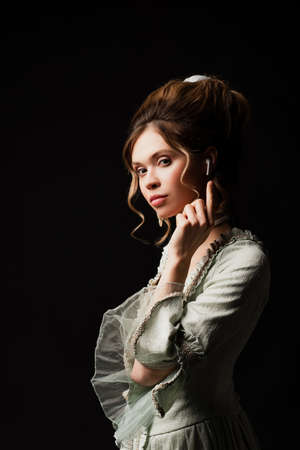 sensual woman in elegant retro outfit listening music and pointing at earphone isolated on blackの写真素材