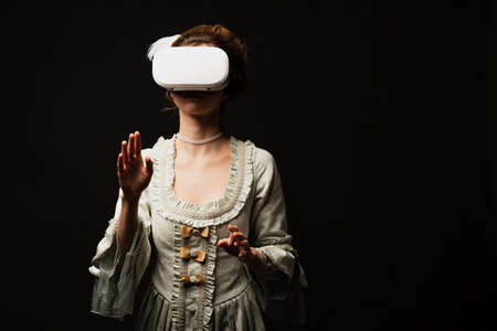 stylish woman in elegant vintage dress gaming in vr headset isolated on black