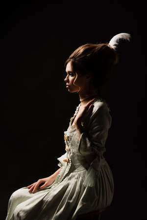side view of charming woman in vintage outfit sitting isolated on black