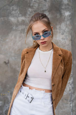 model in blue sunglasses and stylish outfit posing near gray concrete wallの写真素材