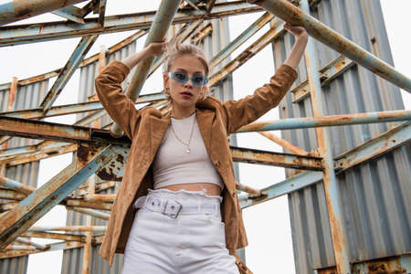 young model in blue sunglasses posing near rusty construction on rooftop