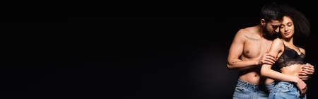 Muscular man hugging gorgeous african american girlfriend isolated on black, bannerの写真素材
