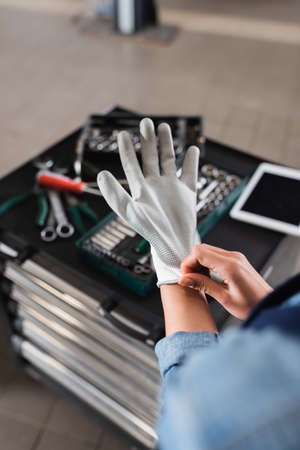 partial view of young mechanic wearing glove on hand near toolbox and digital tablet in auto repair serviceの写真素材